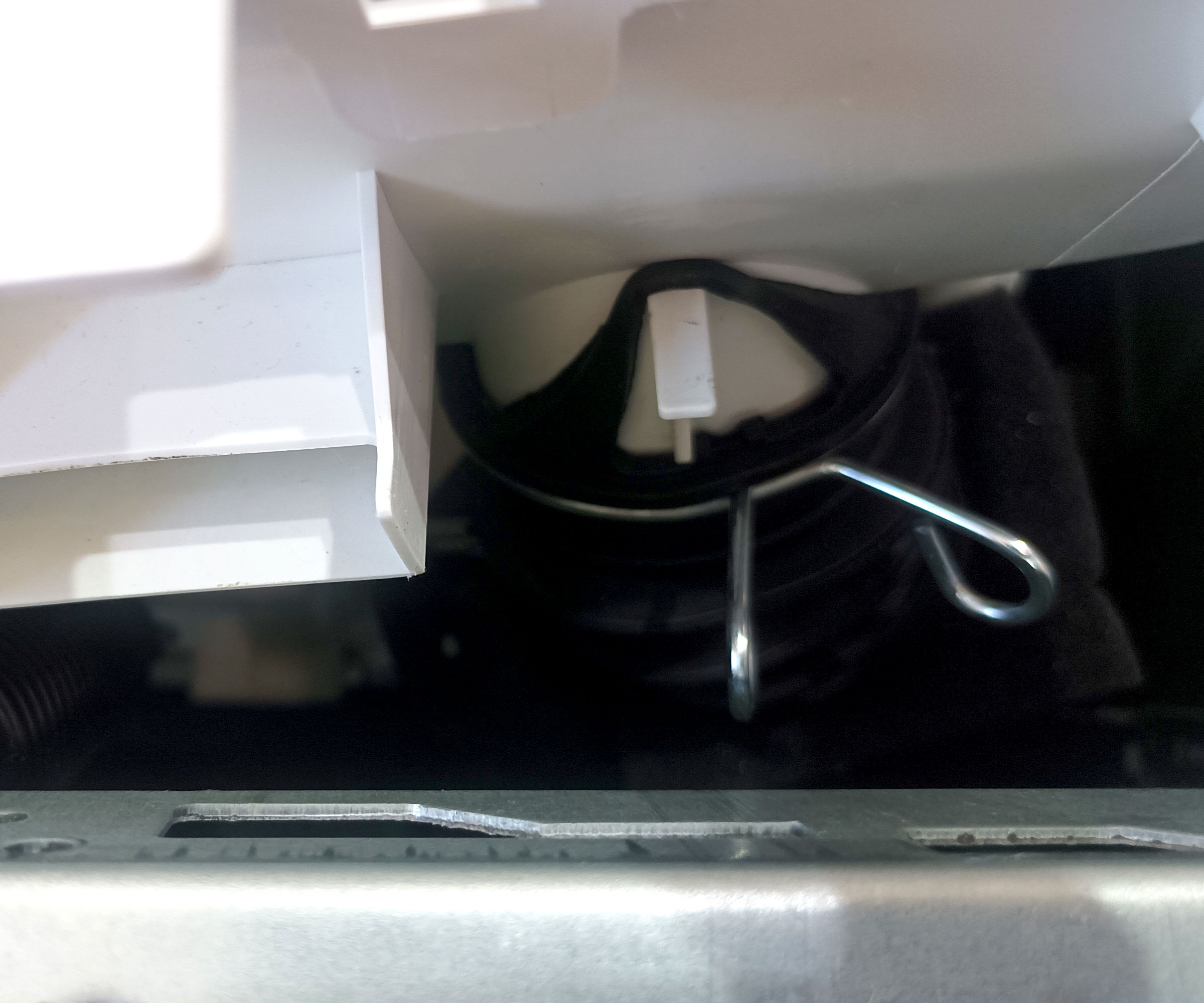 Top down shot of washing machine dispenser hose attached to bottom of detergent tray with holding clip in place.