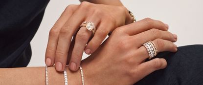 Hands placed on top of each other, wearing various pieces of diamond jewelery
