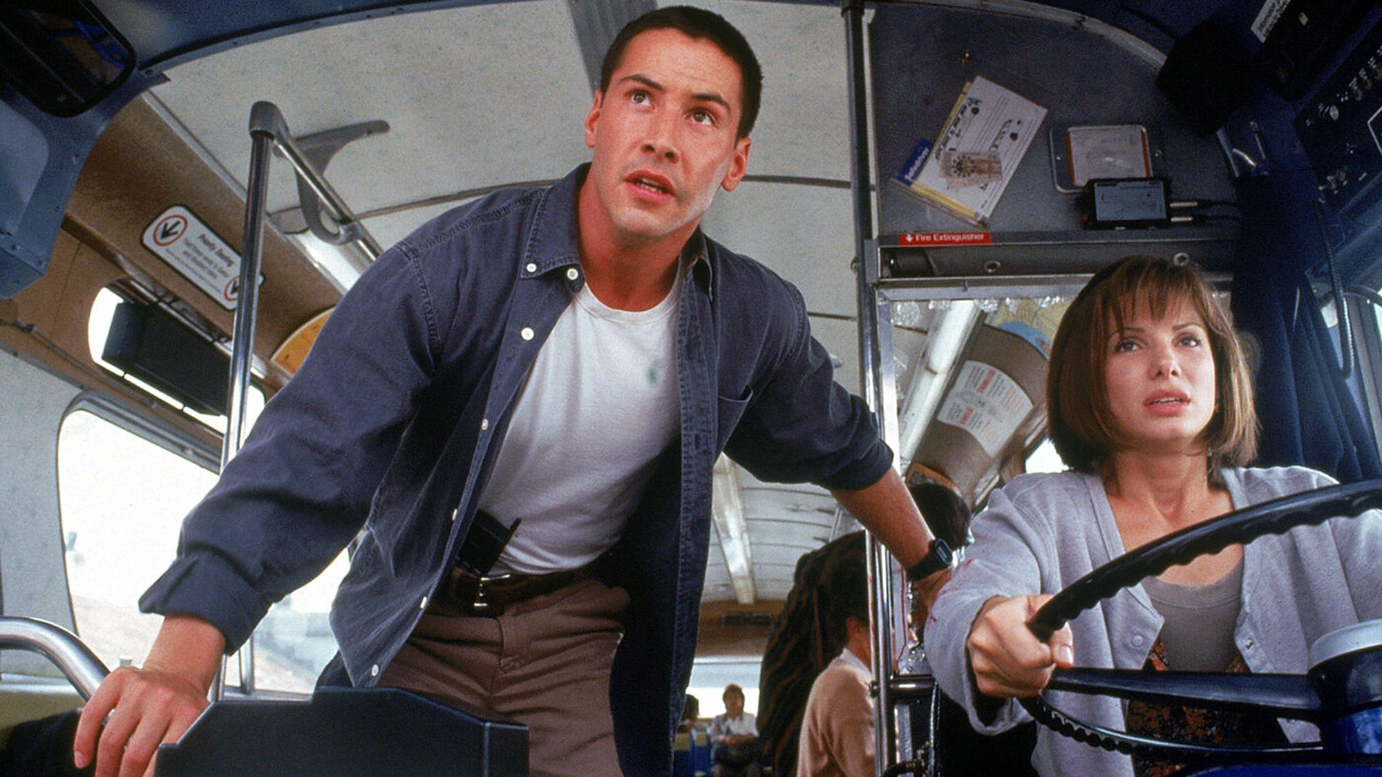 (Von links nach rechts) Keanu Reeves als Jack Traven und Sandra Bullock als Annie Porter, während letztere in „Speed“ den Bus fährt