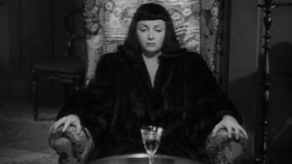 Jacqueline sitting in a chair staring at a glass of poison in The Seventh Victim.