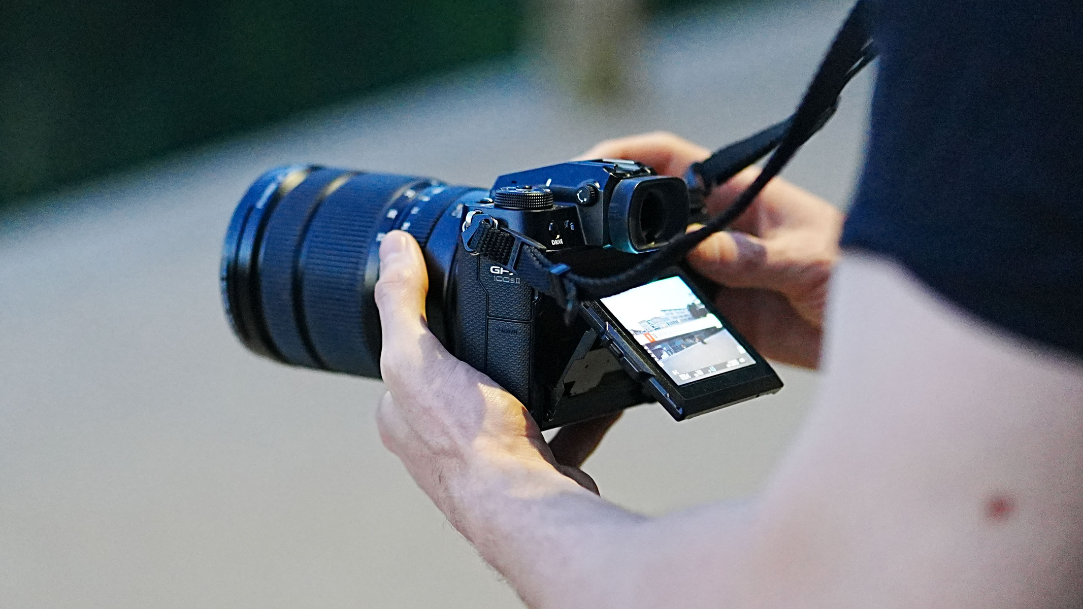 Hands holding the Fujifilm GFX 100S II with the screen tilted upwards.