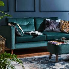 A teal sofa with assorted cushions in a living room with dark panelled walls