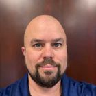 Headshot of Joe Haycock in front of brown wall.