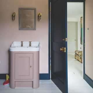 cloakroom design mistakes, pale pink bathroom with inky blue door and skirting, white floorboards, pink painted vanity unit, mirror, wall lights
