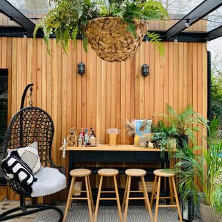 outdoor bench/bar with stools, hanging chair, rattan basket, wall lights, plants