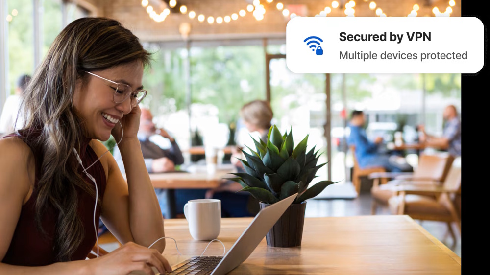 A woman looks happy as you makes a video call in a café in a promotional image for Norton VPN.