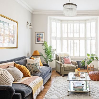 living room with navy sofa and cushions, coffee table on rug, and bay window with shutters