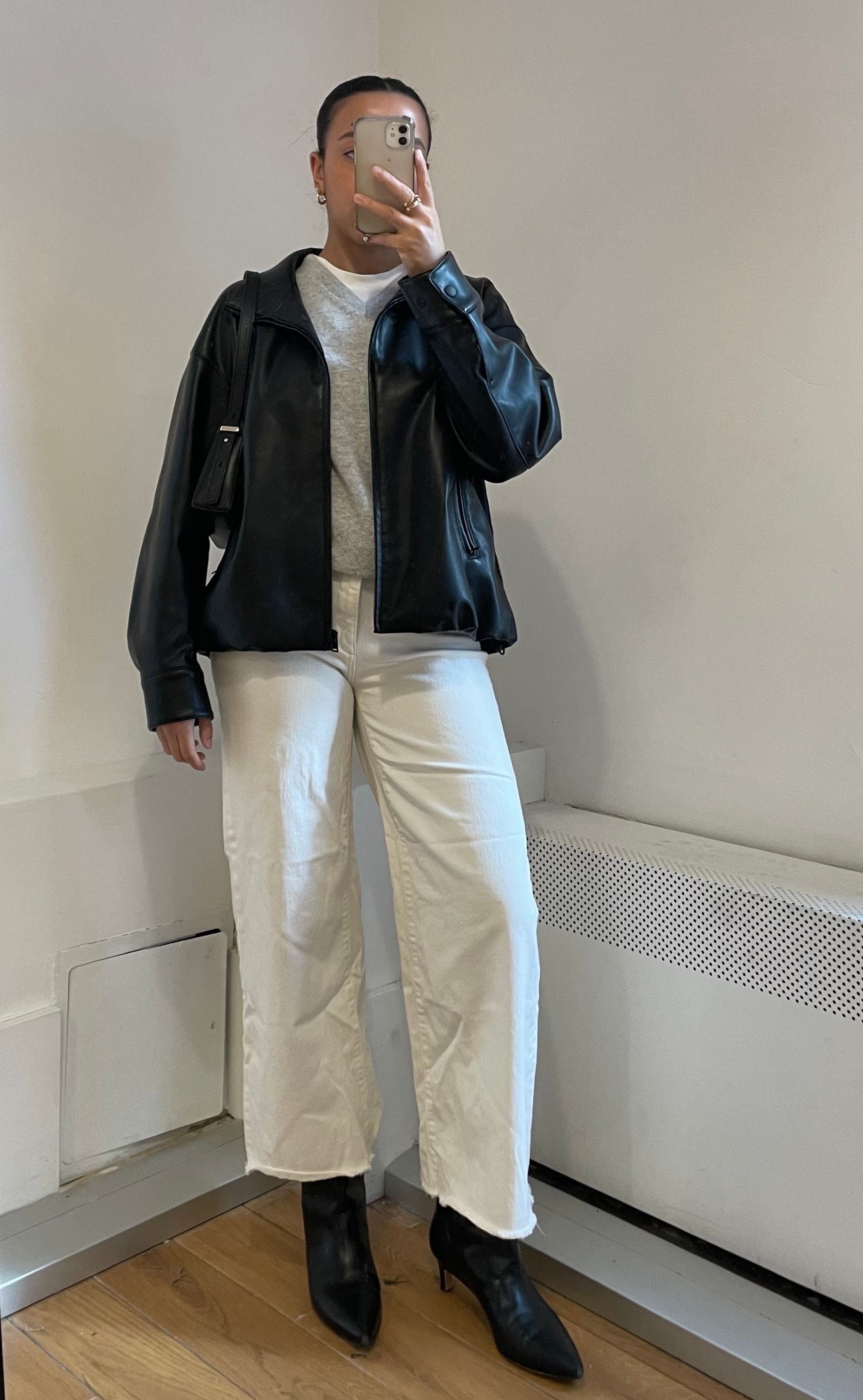 Lauren Tappan wearing a black leather jacket, white jeans, a sweater vest, boots, and a shoulder bag