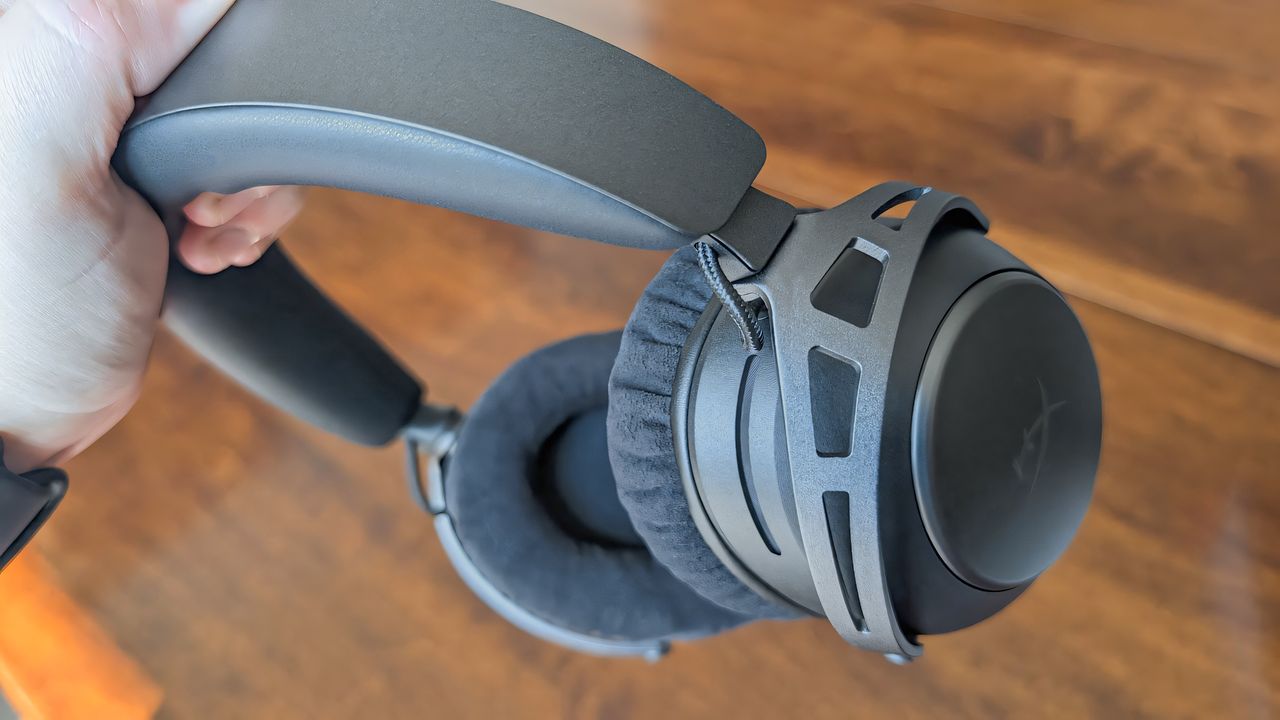 A hand holding the HyperX Cloud Alpha 2 Wireless gaming headset by the headband.