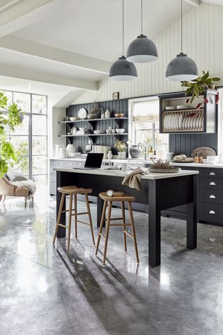 A black kitchen island with wooden bar stools and gray pendant lights