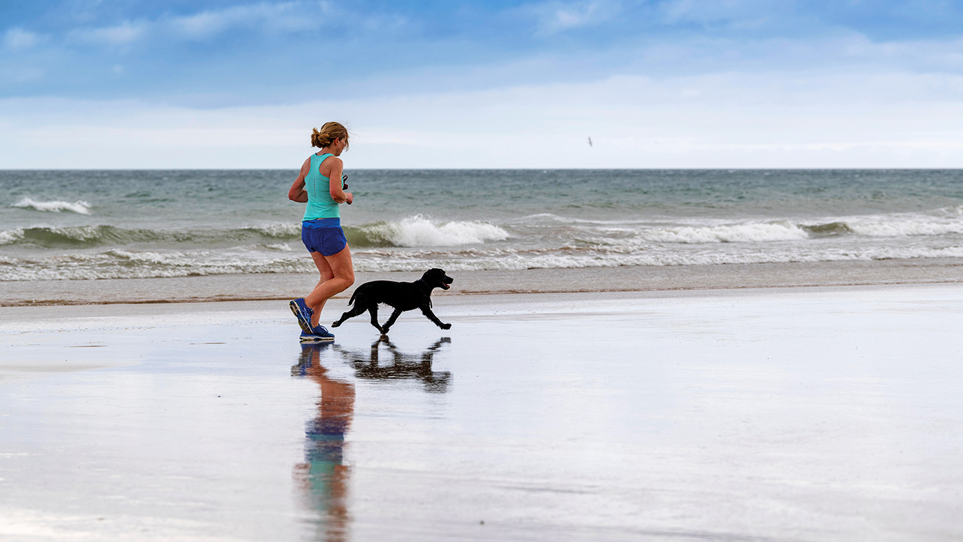 WR5D3P Woman jogging on Benone Beach with her dog, Northern Ireland, UK.