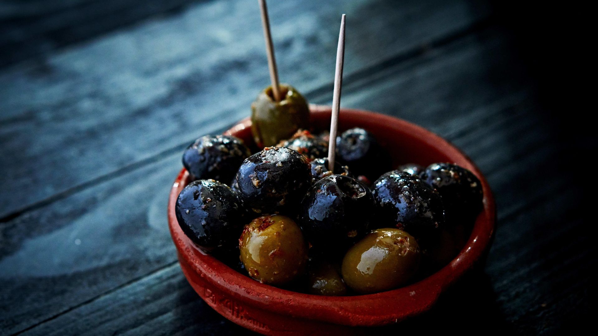 A small tapas bowl full of green and black olives