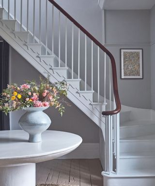 A fresh country look. Entrance hall with white wooden stairway and flower bouquet on round table.