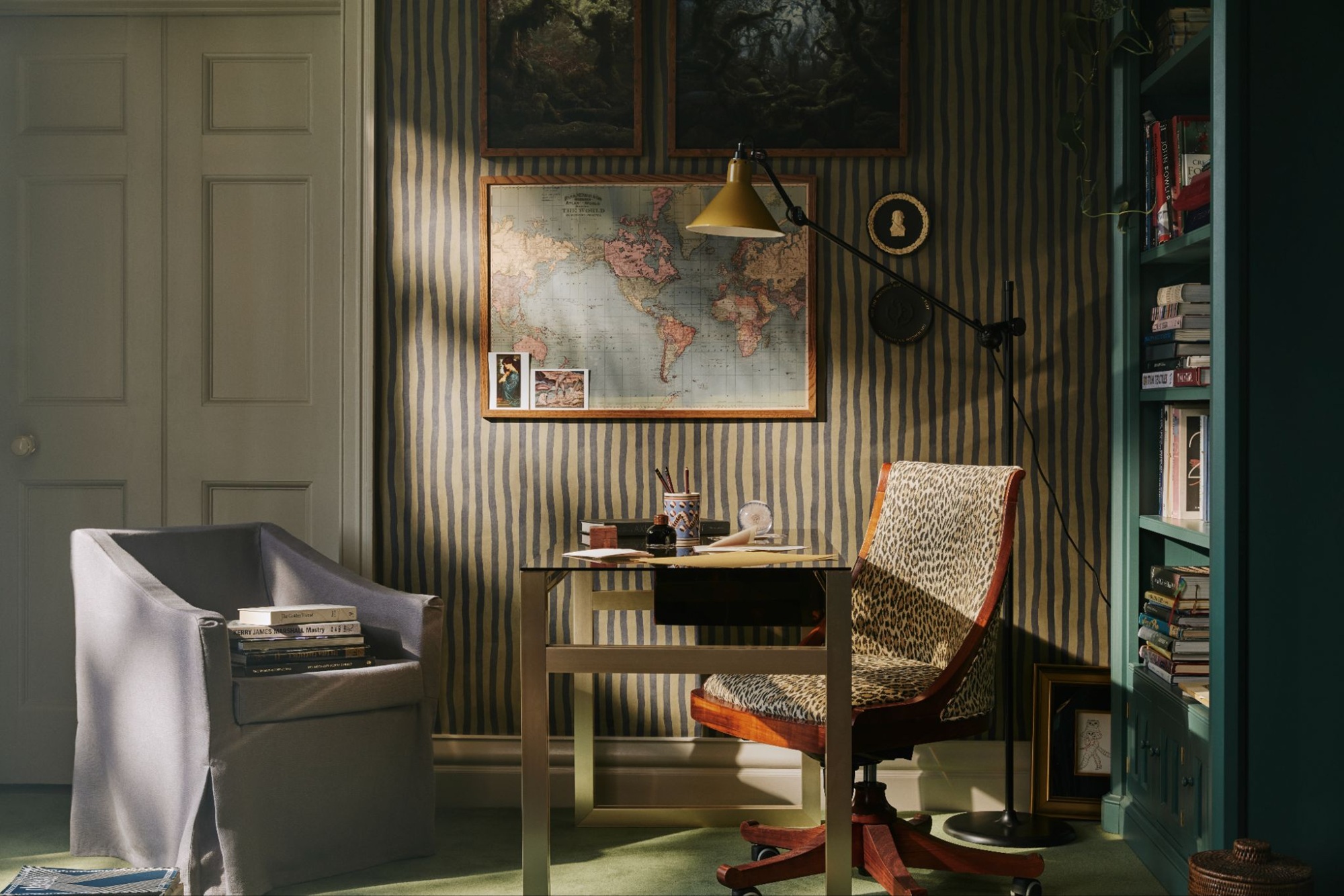 a study with a green striped wallpaper and a small desk
