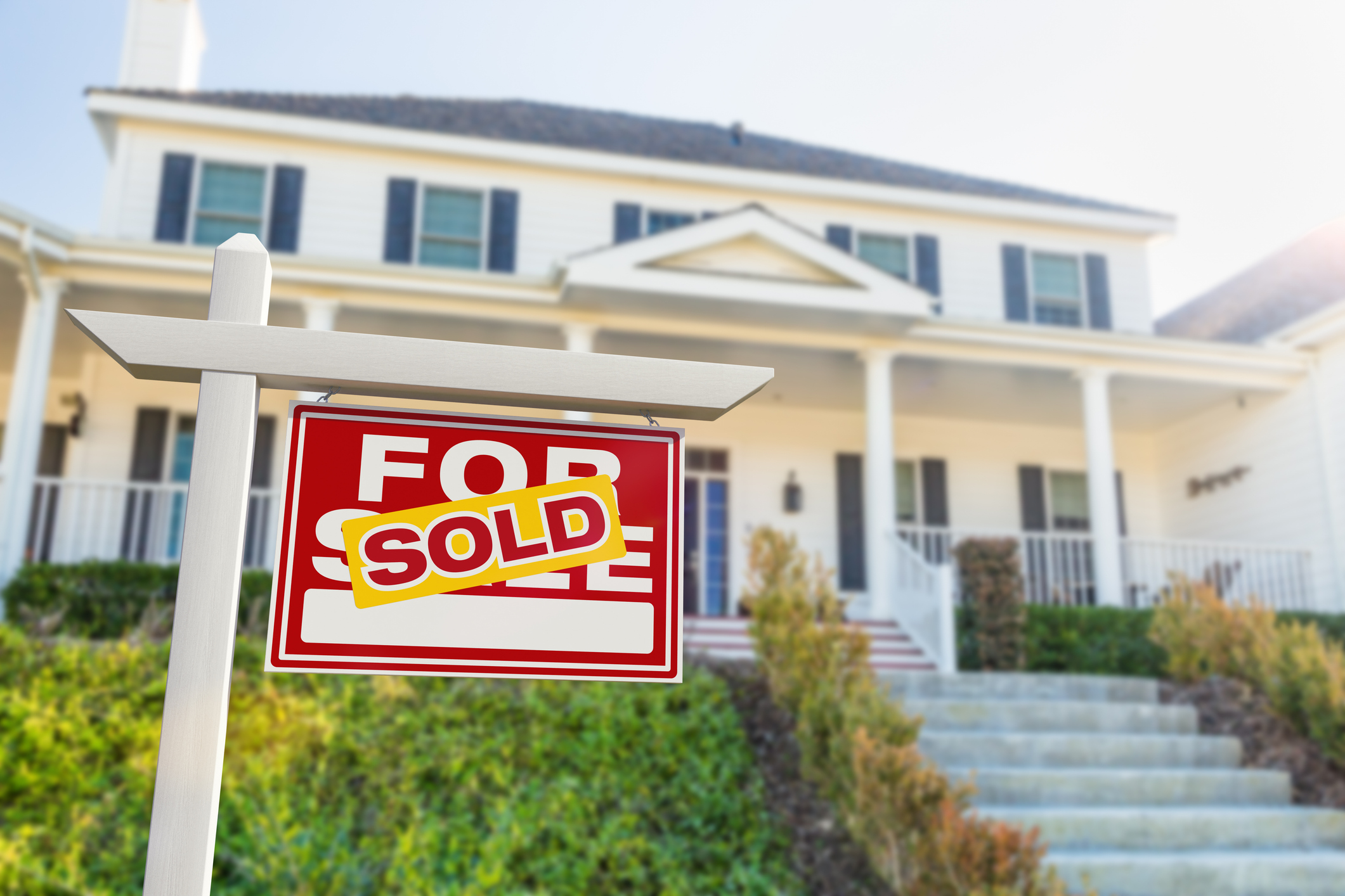 A For Sale sign with a SOLD sticker on it. In front of a home