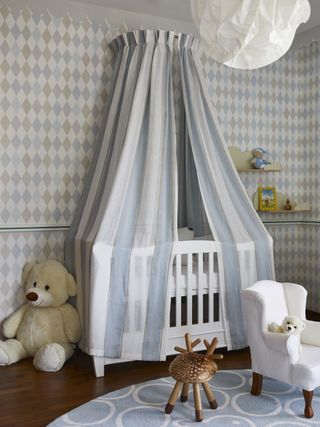baby boy nursery with blue stripe canopy over crib, harlequin style wallpaper, hardwood floor, rug, toys