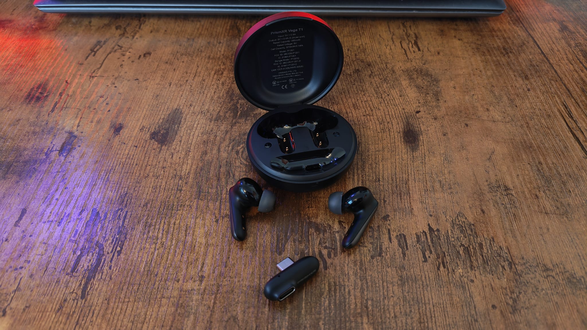 The case for the PrismXR Vega T1 earbuds open with the USB dongle and earbuds lying next to it