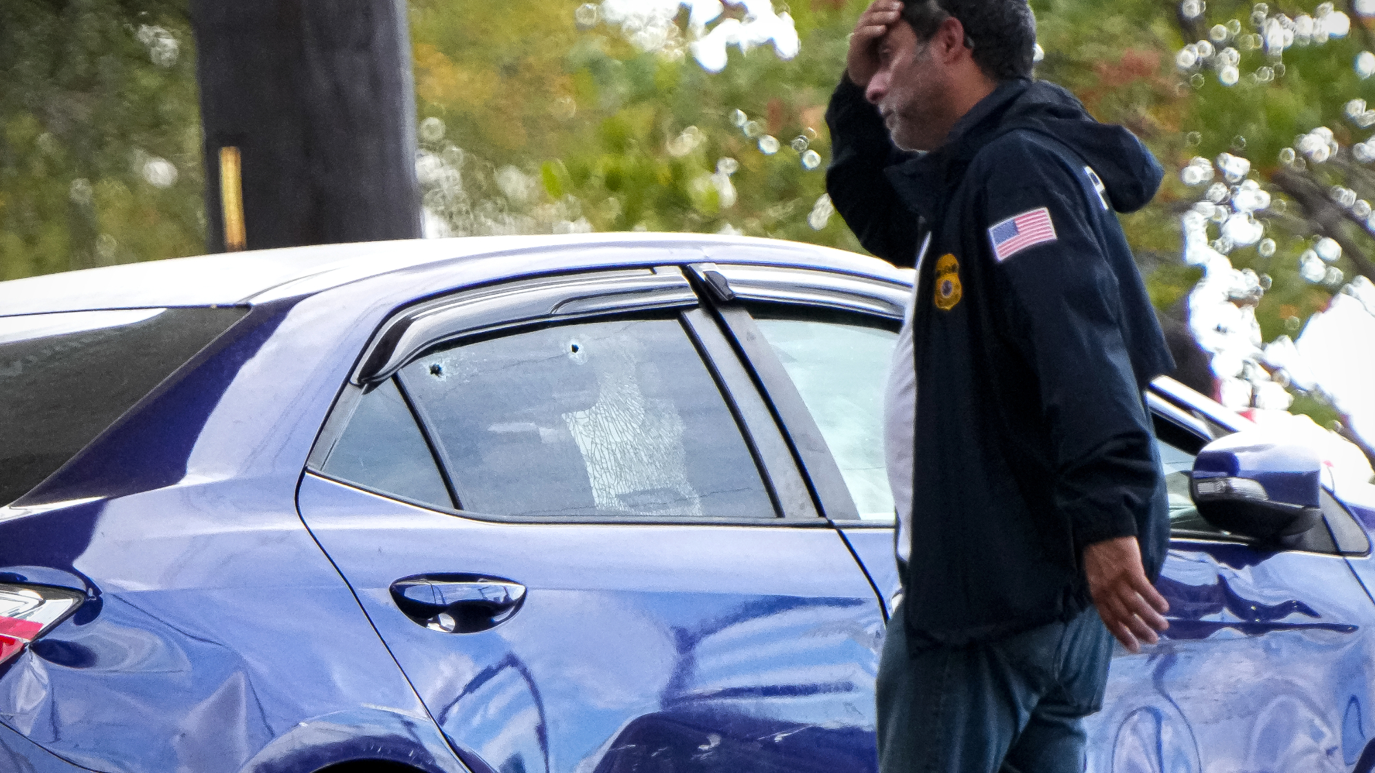 A federal agent walks past vehicle with a damaged door and bullet holes in a broken window after an I.C.E. shooting in Austin, Texas.