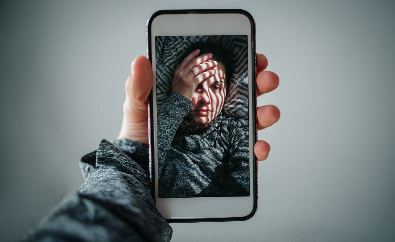 Cropped Hands Of Woman Holding Mobile Phone While Taking Selfie Against Grey Background. Is Instagram bad for mental health?