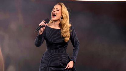 Adele performs onstage in Munich wearing a blue black dress and large hoop earrings