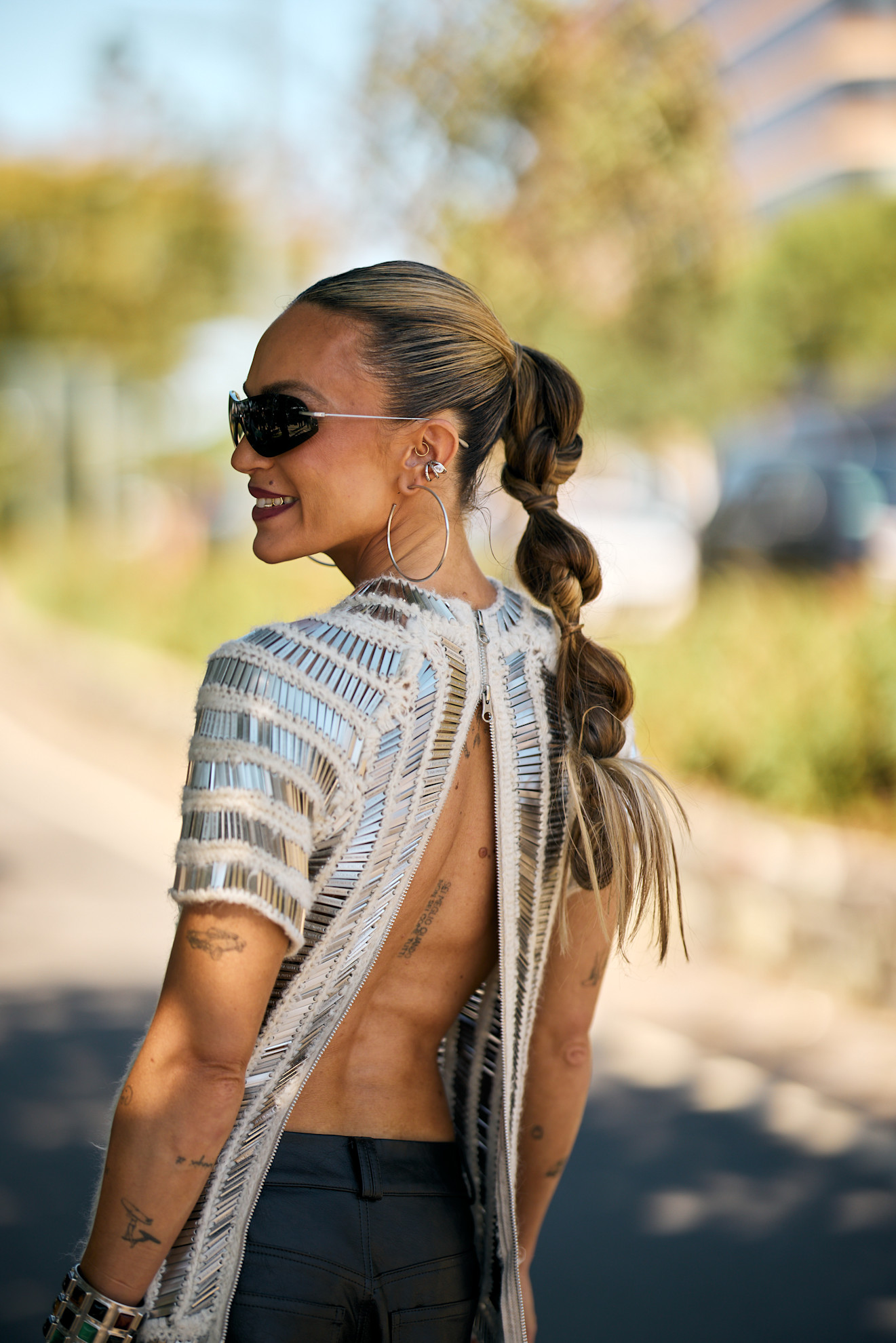 a woman with a silver open back shirt, blonde ponytail and sunglasses