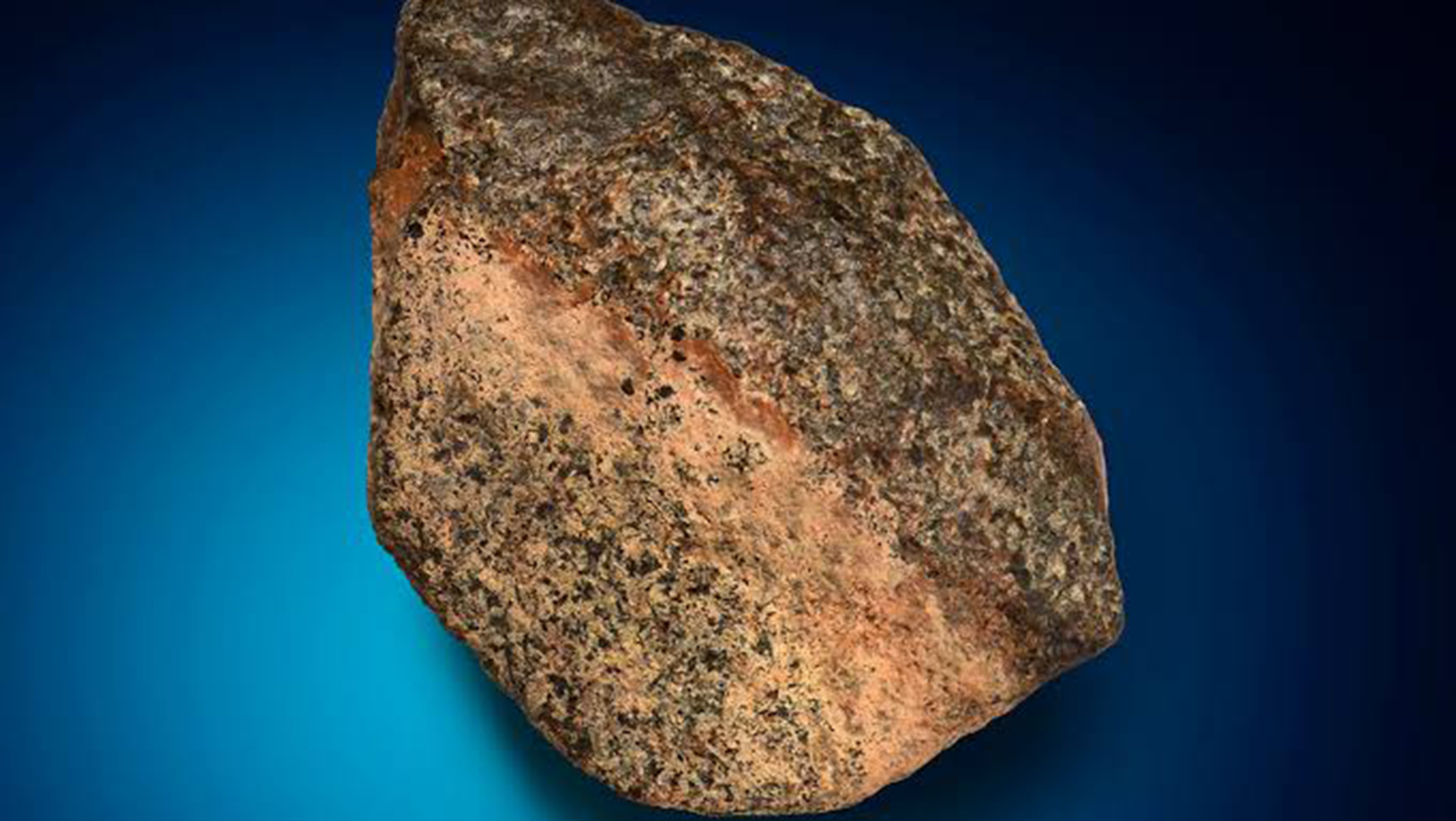 A close up of a large reddish rock against a blue background