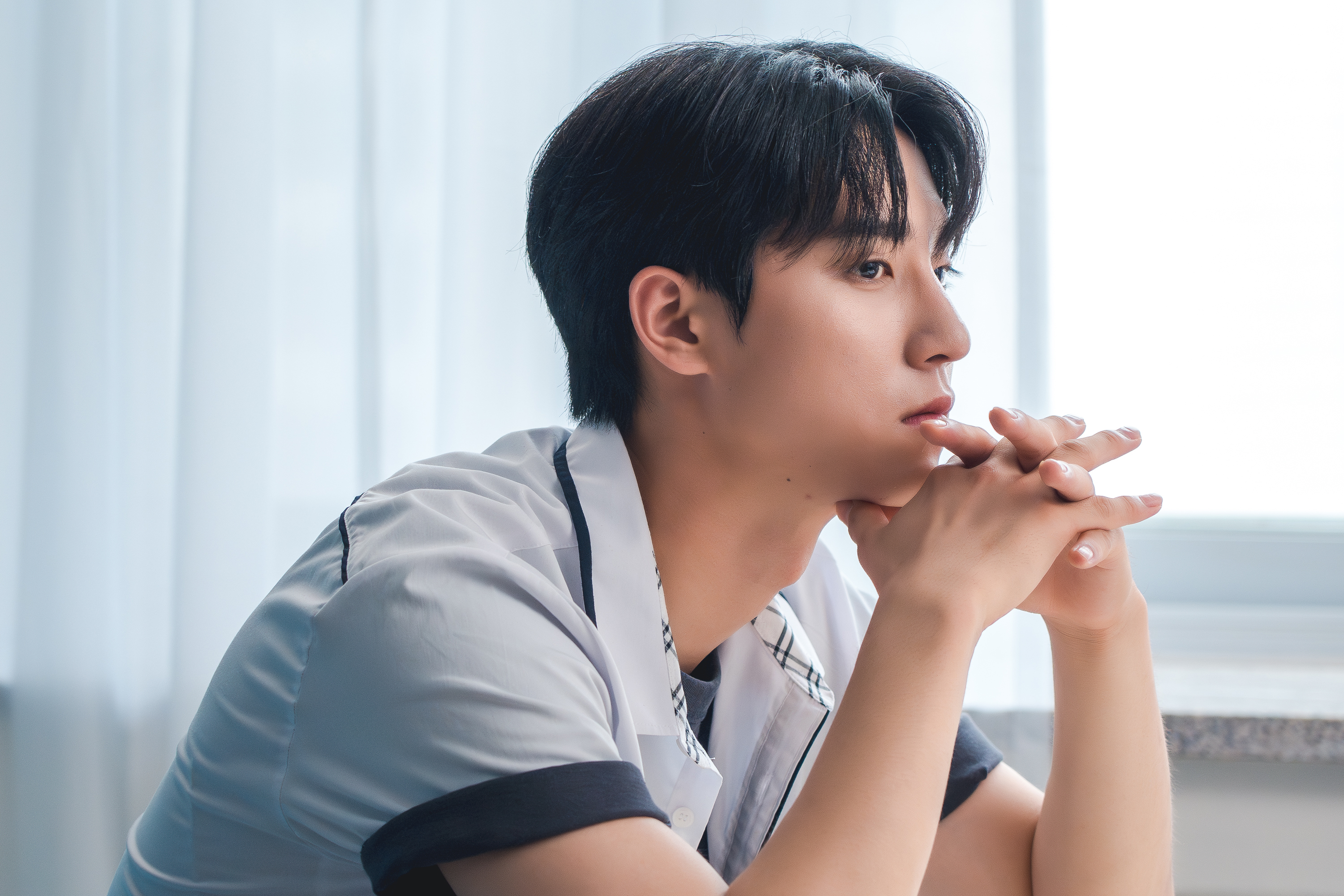 a man sits and rests his chin in his hands in a still from the bl kdrama jazz for two