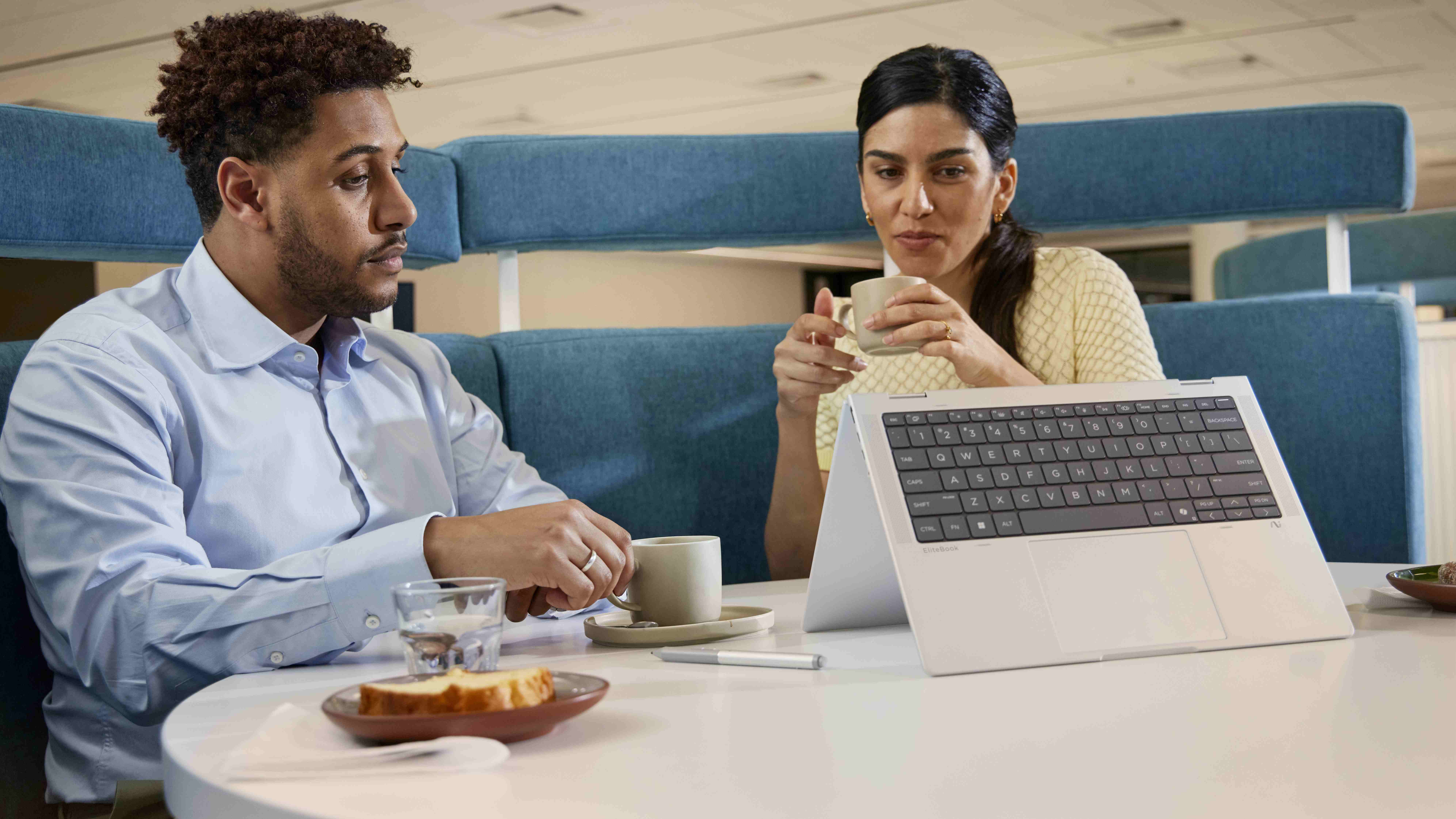 Two people seated at a table with the HP EliteBook X Flip 14 (G1i) in tent mode on the table in front of them.