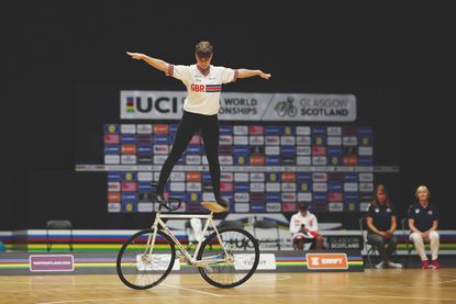 Katarina Howe on moving bike standing one foot on the bars, one foot on the handlebars