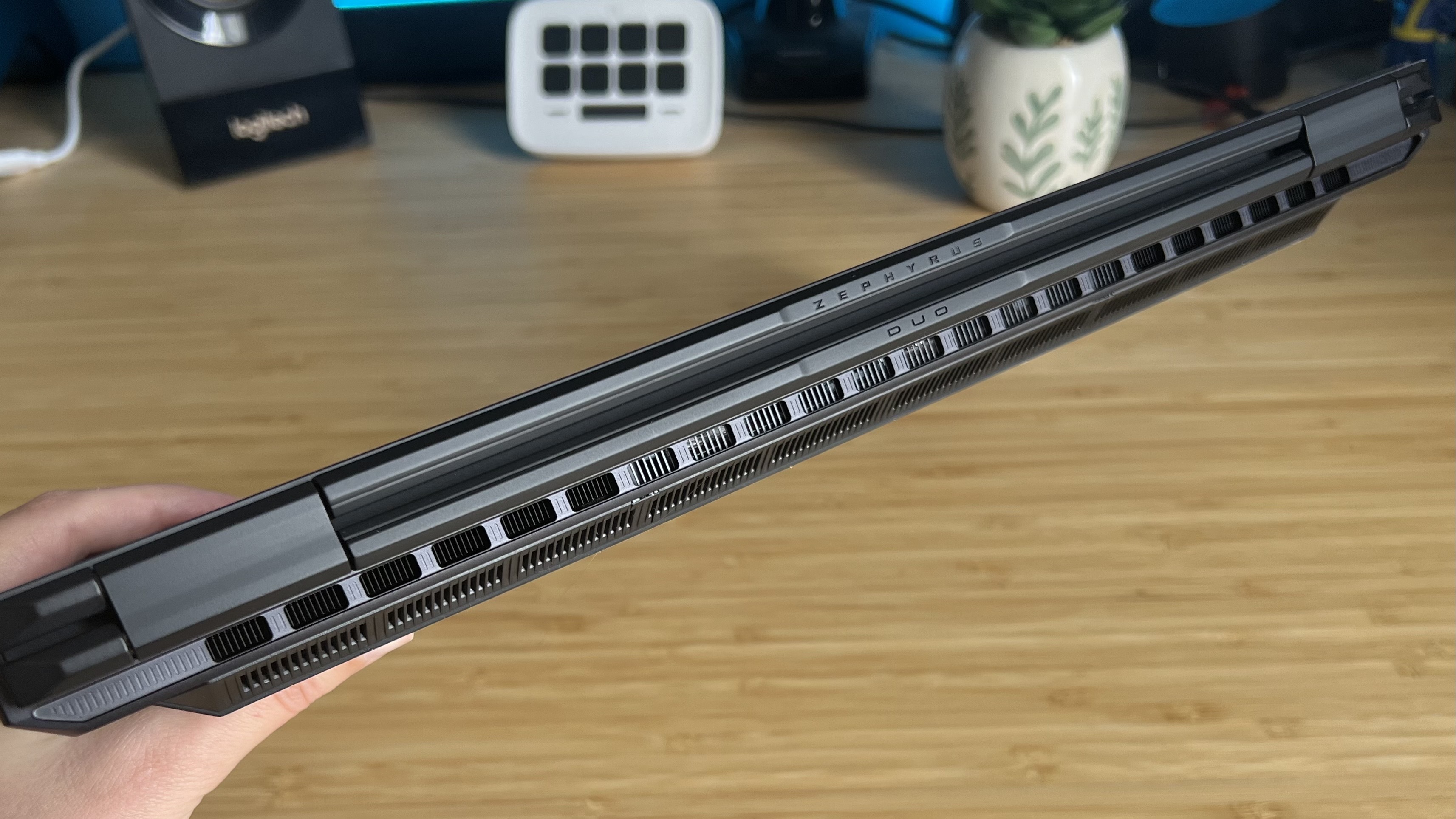 Hand holding closed Asus ROG Zephyrus Duo gaming laptop with exhaust grills easily visible along the back