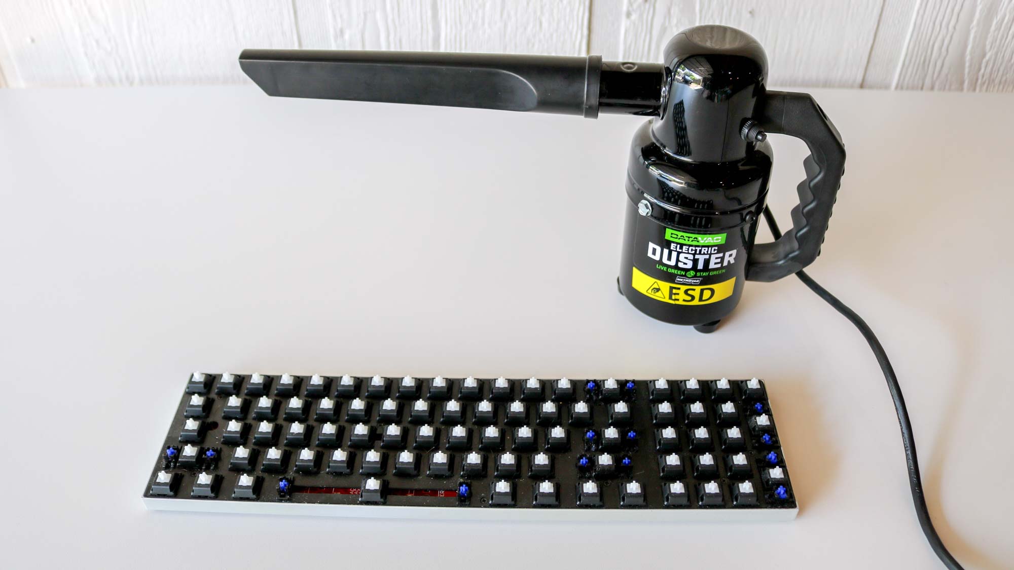 A keyboard without keycaps next to an electric duster