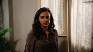 Sara Vickers in a dark patterned blouse stands near a door in Endeavour