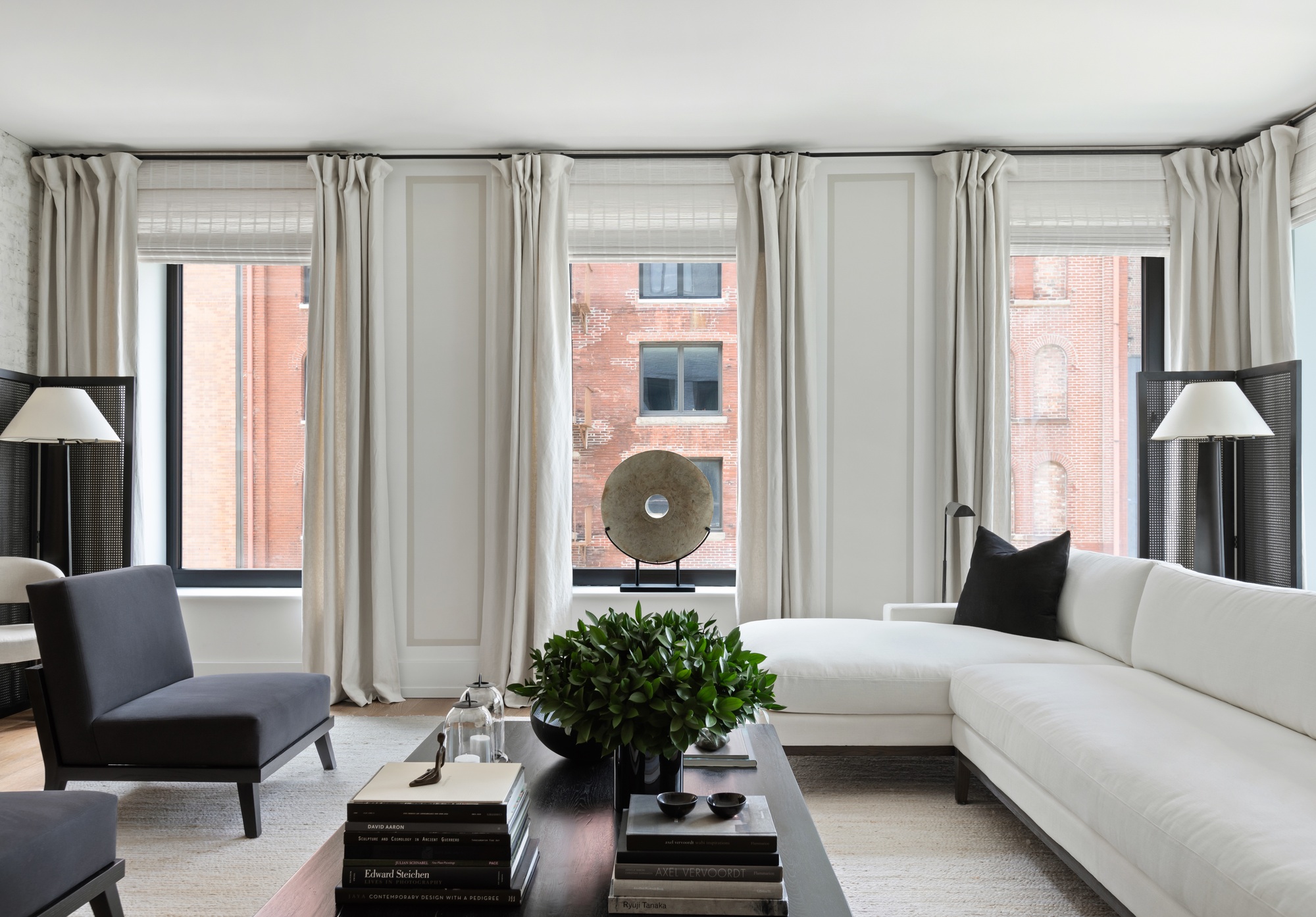 A large neutral living room with a white L-shaped sofa, black coffee table, and three tall windows