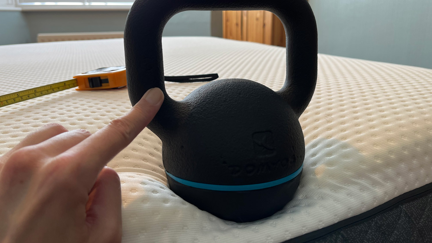 A kettlebell on the edge of the Emma NextGen Premium with a finger holding it in place