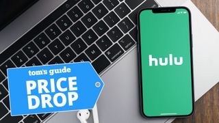 Hulu logo shown on iPhone lying on MacBook laptop