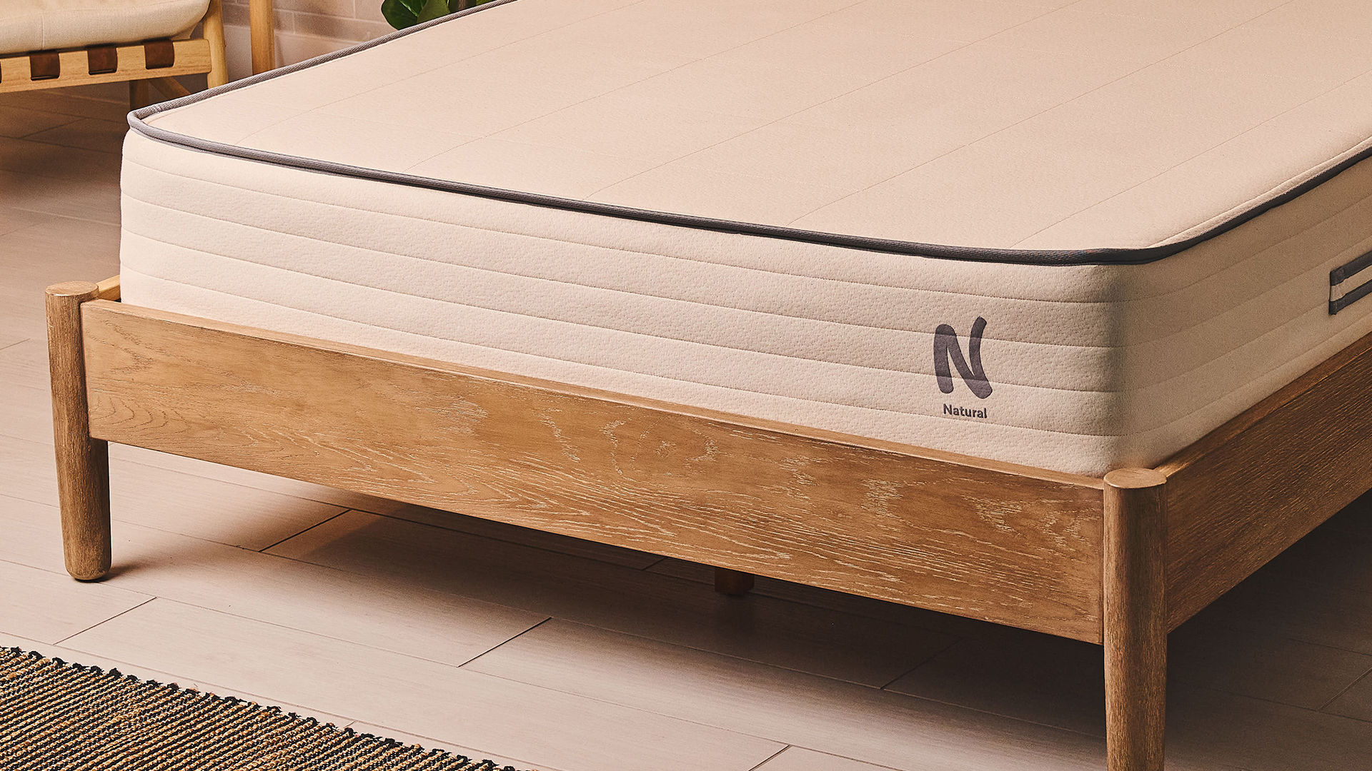 A close-up of the foot of the Nolah Natural 11 Mattress displaying the Nolah logo, on a bed frame in a bedroom