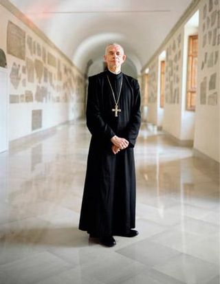 Priest in black robes stood in marble-like cloisters