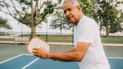 An older man playing pickleball prepares to serve