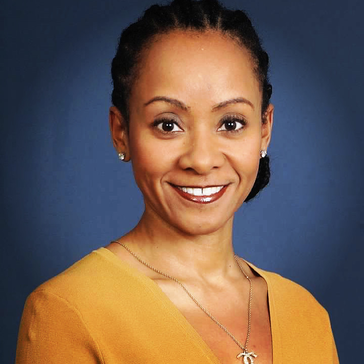 a black woman in a mustard yellow top with a Chanel necklace