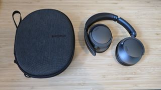 A pair of dark grey and black 1More Sonoflow headphones sitting on a wooden table