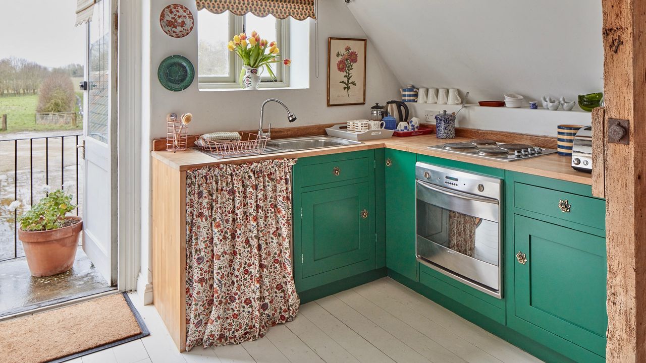 A green kitchen with a floral curtain covering the under-sink storage space