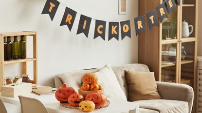 Prime Day Halloween décor: A beige living room with a halloween banner and pile of pumpkins on the table