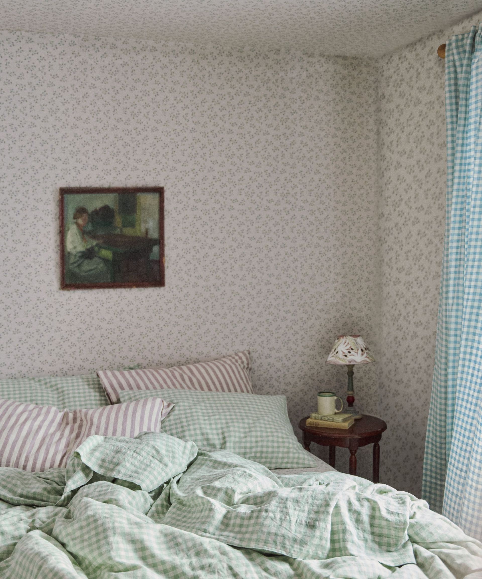 cottage bedroom wallpapered in ditsy floral wallpaper with gingham and striped bedding and antique art