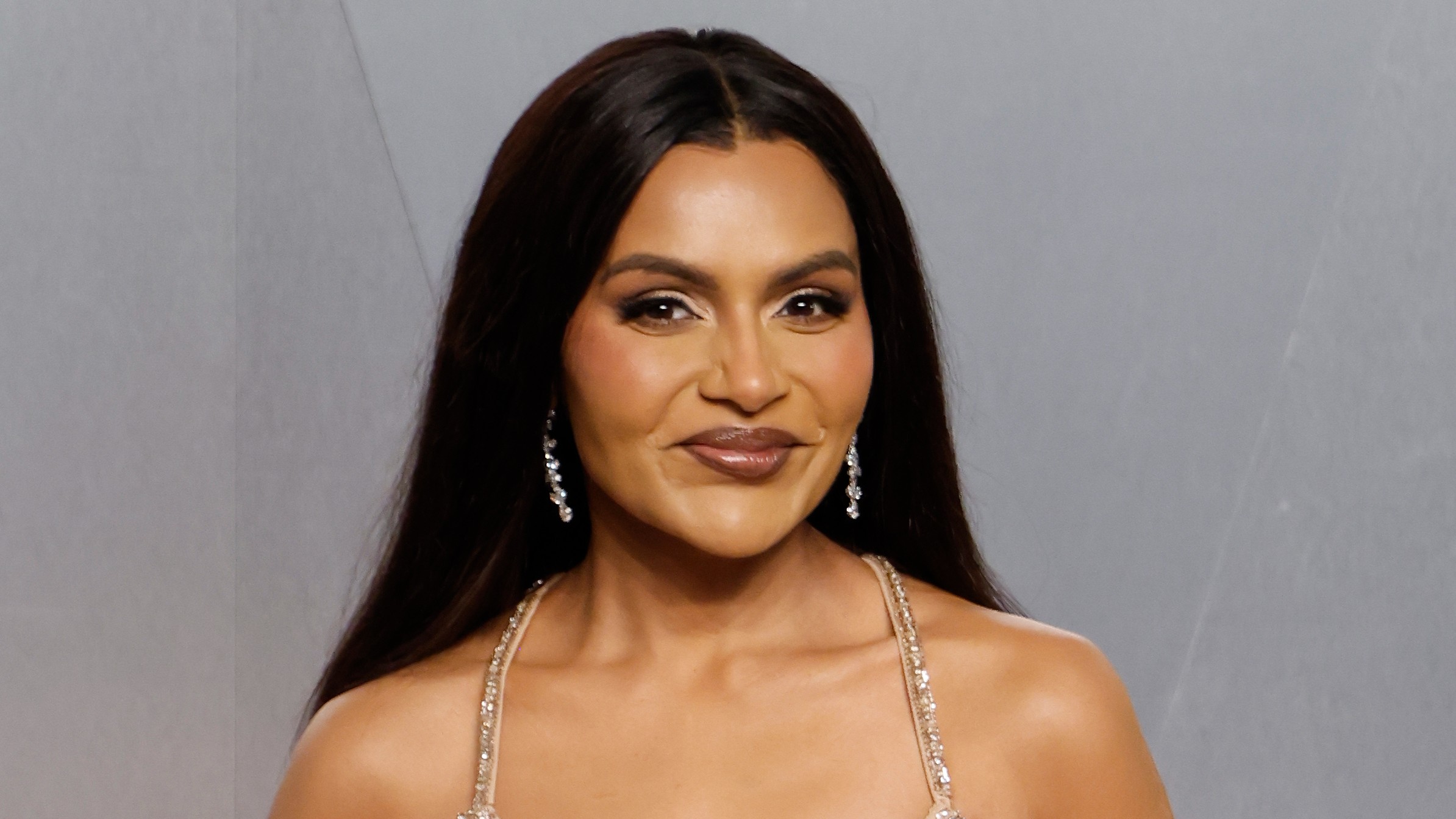 a woman with dark hair poses in front of a gray background at a red carpet event