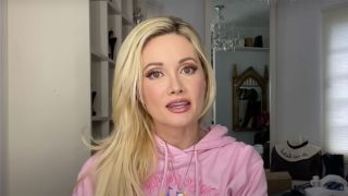 Holly Madison talks into the camera, wearing a pink sweater.