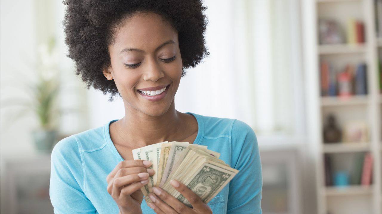 A smiling young woman hands some cash that&#039;s fanned out like a hand of playing cards.