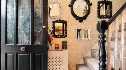Small entryway mirror ideas are so useful for creating intrigue. Here is an entryway with a gallery mirror wall, a stair case with black and white spindles, and a black door