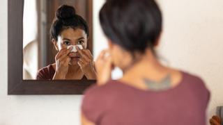 A woman applying a white nasal strip in the mirror