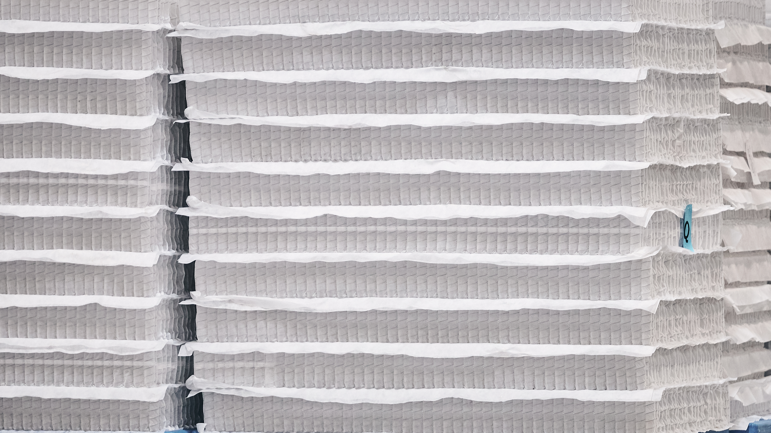 The image shows rows and rows of pocketed mattress coils piled up in a mattress factory