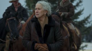 Helen Mirren as Cara standing in front of two cowboys on horses. 